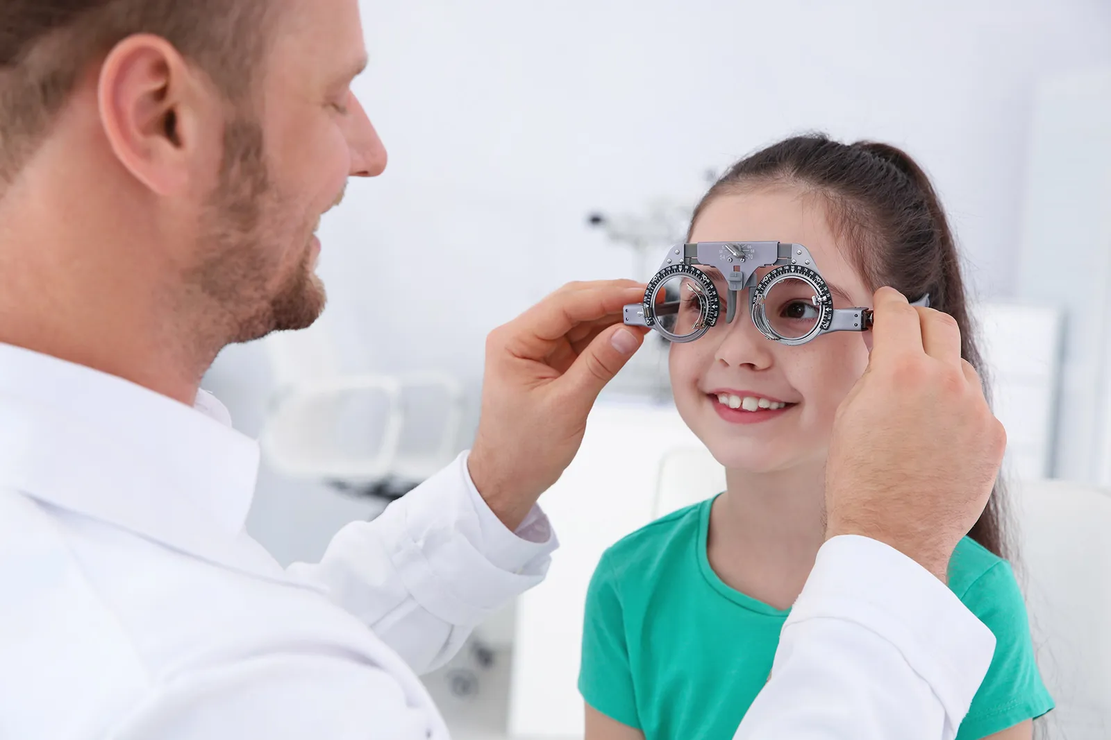 A smiling girl in a trial frame while the optometrist adjusts it
