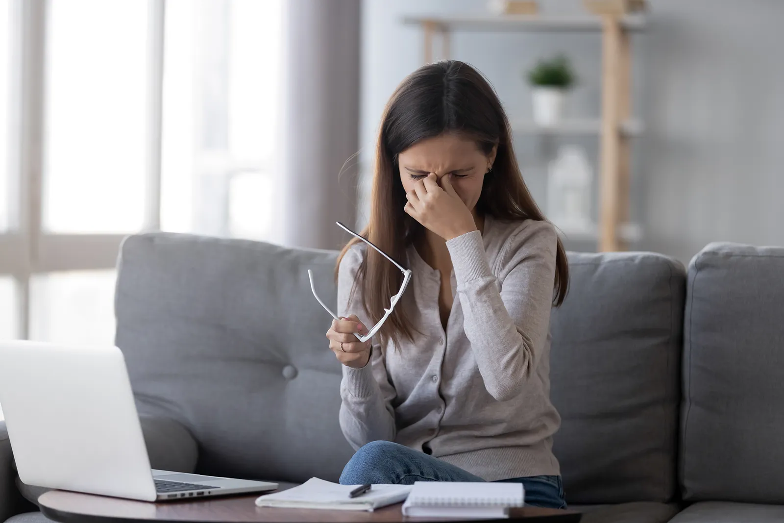 A woman holding her glasses and pressing the bridge of her nose with sore, dry eyes