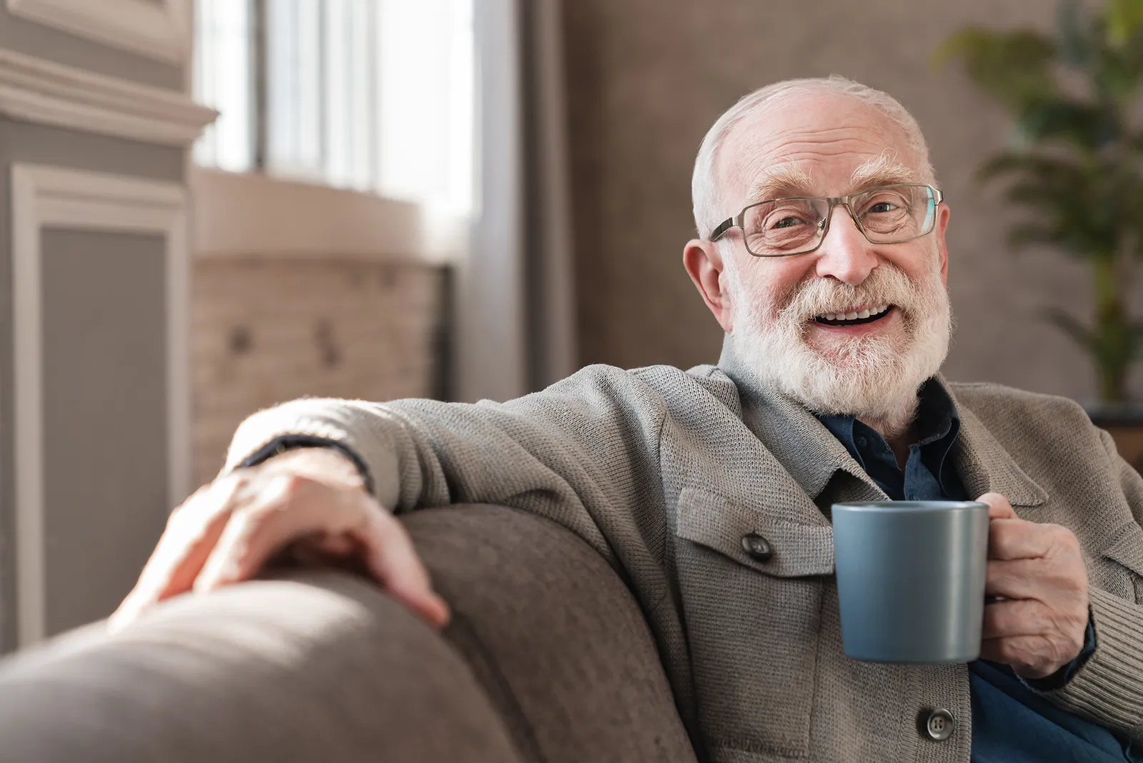 A smiling older man in glasses relaxing with a mug of tea at home