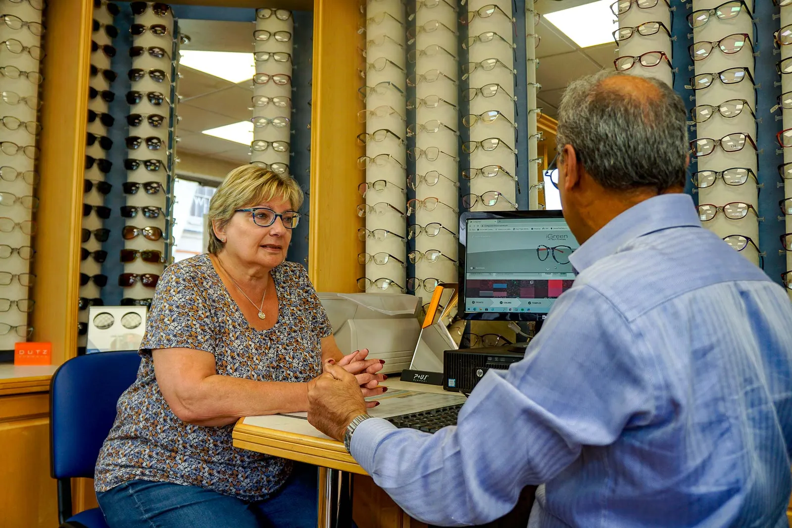 A patient discussing her eyewear in front of the Nu-Sight frame wall